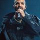 Drake performing on stage in a dark jacket, holding a microphone