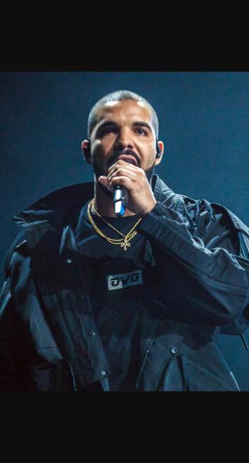 Drake performing on stage in a dark jacket, holding a microphone
