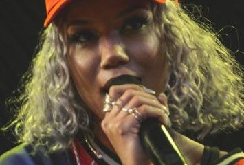 Jhené Aiko performing on stage wearing an orange cap