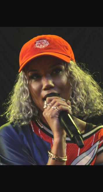 Jhené Aiko performing on stage wearing an orange cap